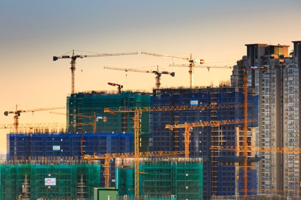building-canes-2138126 A cityscape featuring high-rise buildings under construction with cranes during sunset.