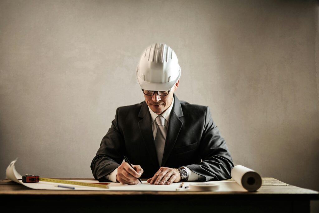 pexels-photo-3771045-3771045 Engineer in a suit drafting architectural plans at a desk indoors.